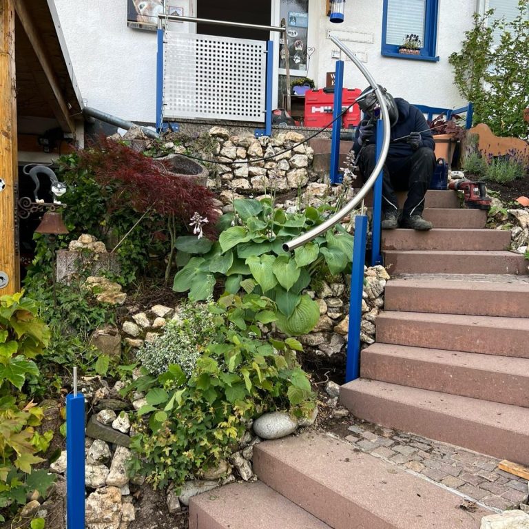 Stufen mit Pflanze und Handlauf vor einem Haus, Person sitzt auf den Stufen.